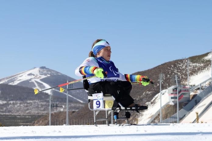A female Paralympic sit-skier is racing in front of mountains